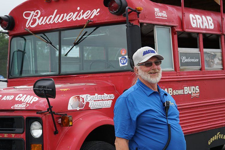 A man is standing in front of a red budweiser bus