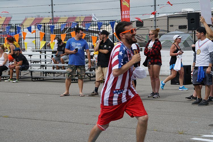A man in an american flag shirt and shorts is running in a parking lot.