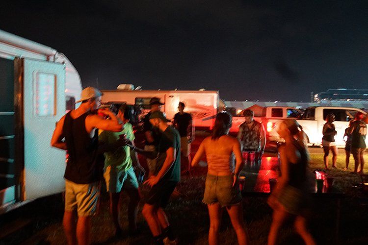 A group of people are standing in a parking lot at night.