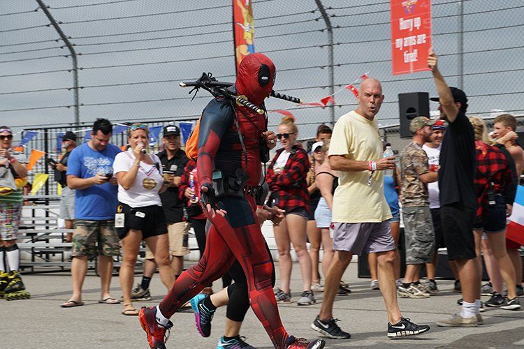 A man in a deadpool costume is walking through a crowd of people.