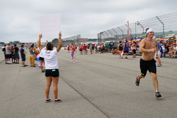 A woman holding a sign stands next to a man running on a race track