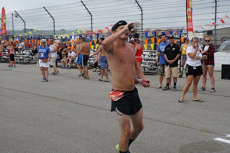 A shirtless man is walking on a race track while a crowd watches.