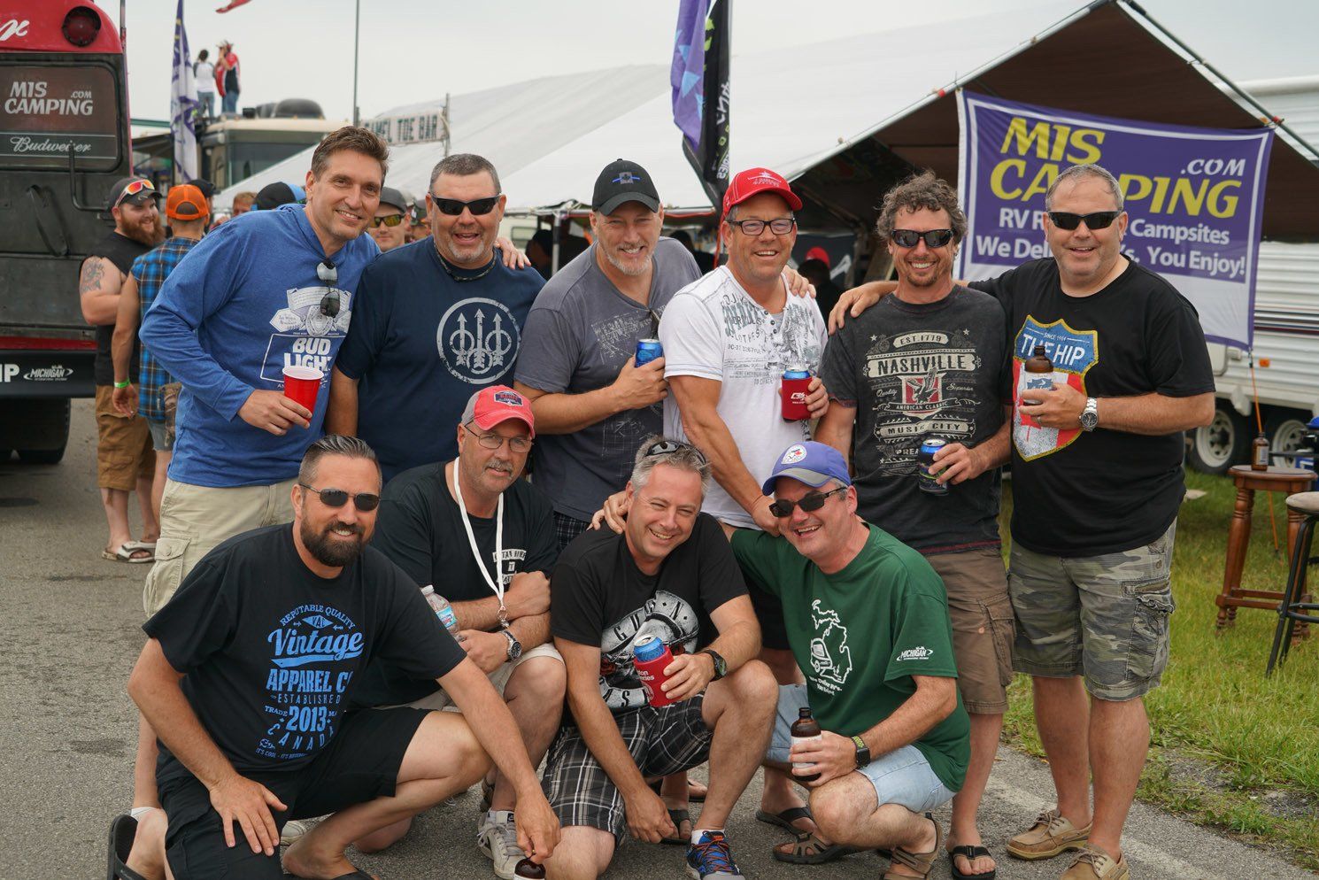 A group of men posing for a picture in front of a mis camping sign