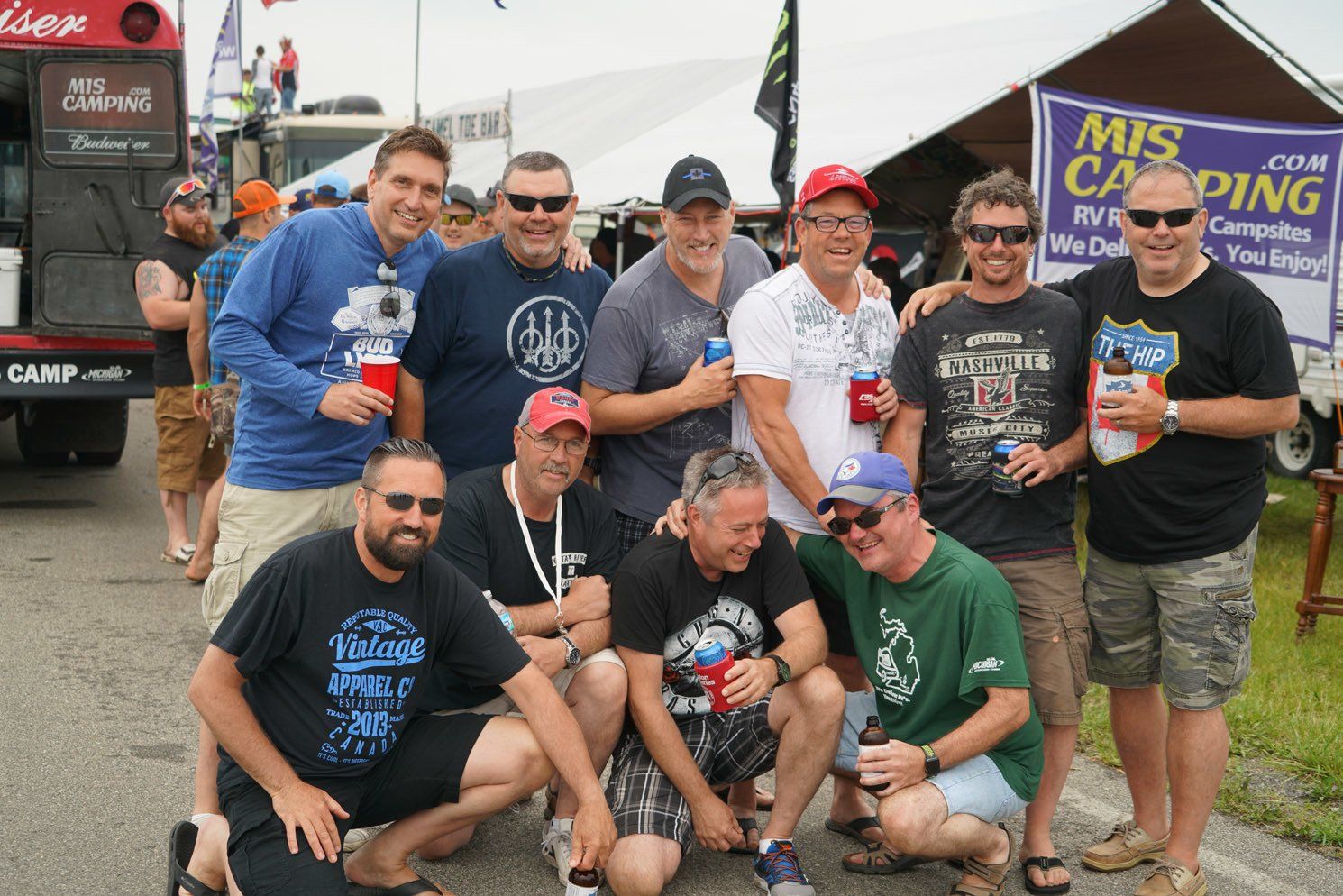 A group of men posing for a picture in front of a sign that says mis camping