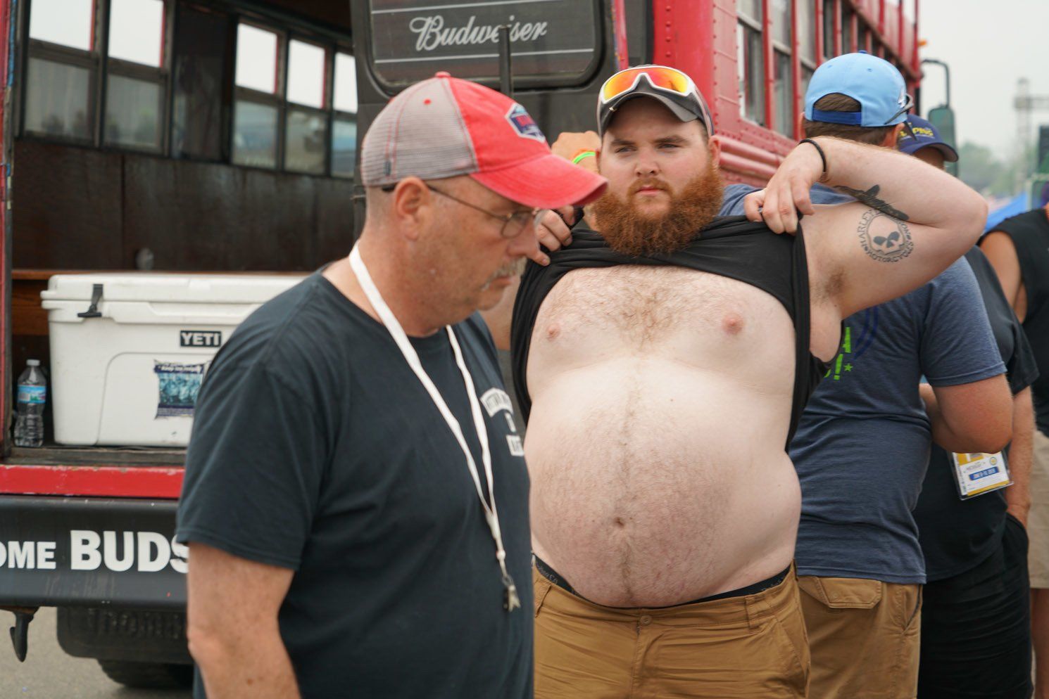 Two men are standing next to each other in front of a budweiser bus.