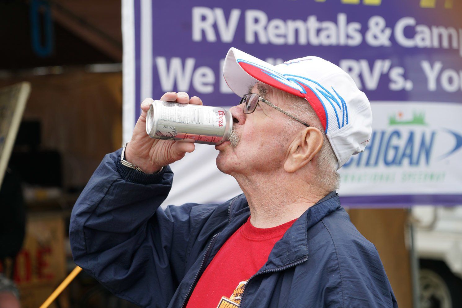 A man drinking from a can in front of a sign that says rv rentals