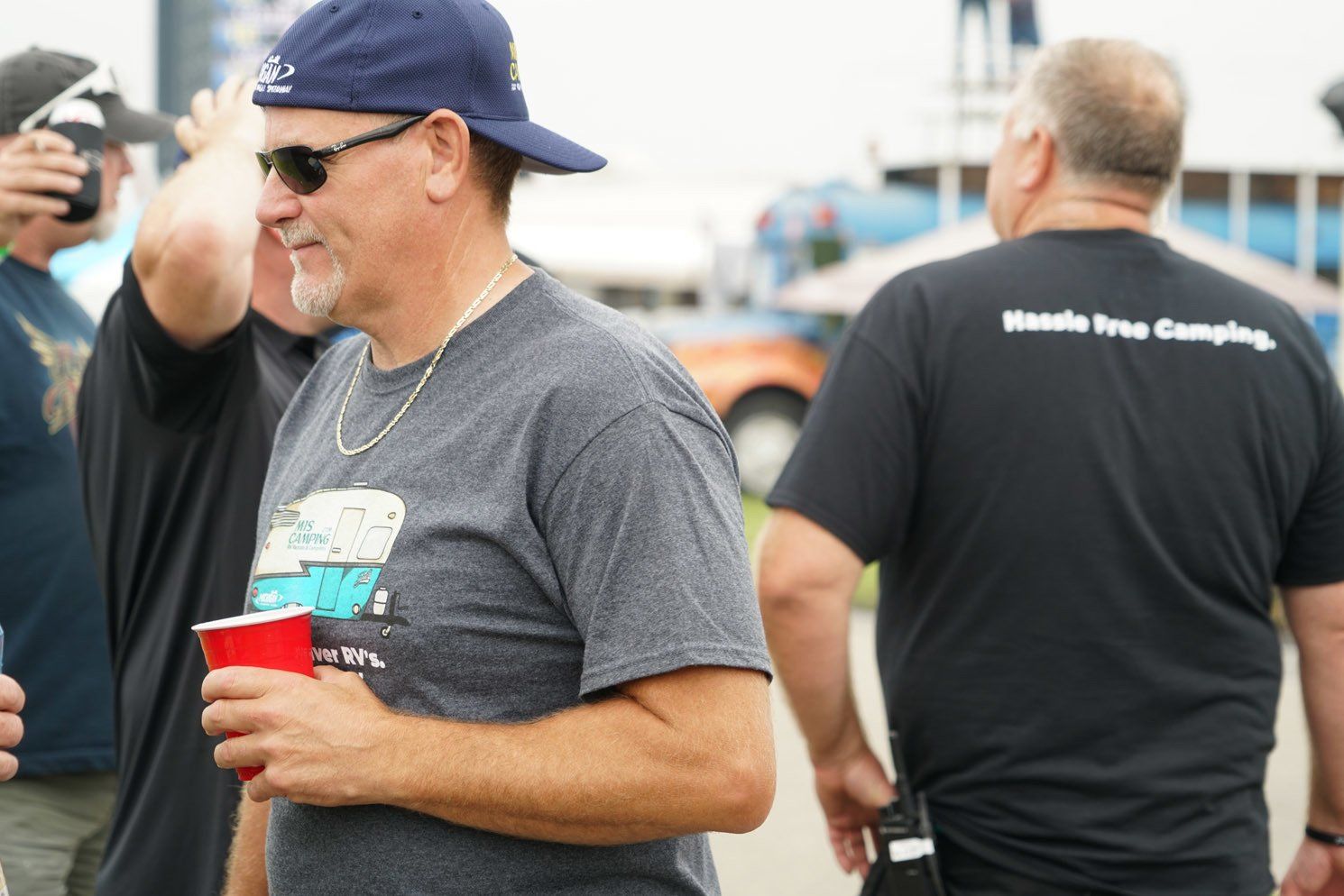 A man wearing a hat and sunglasses is holding a red cup.