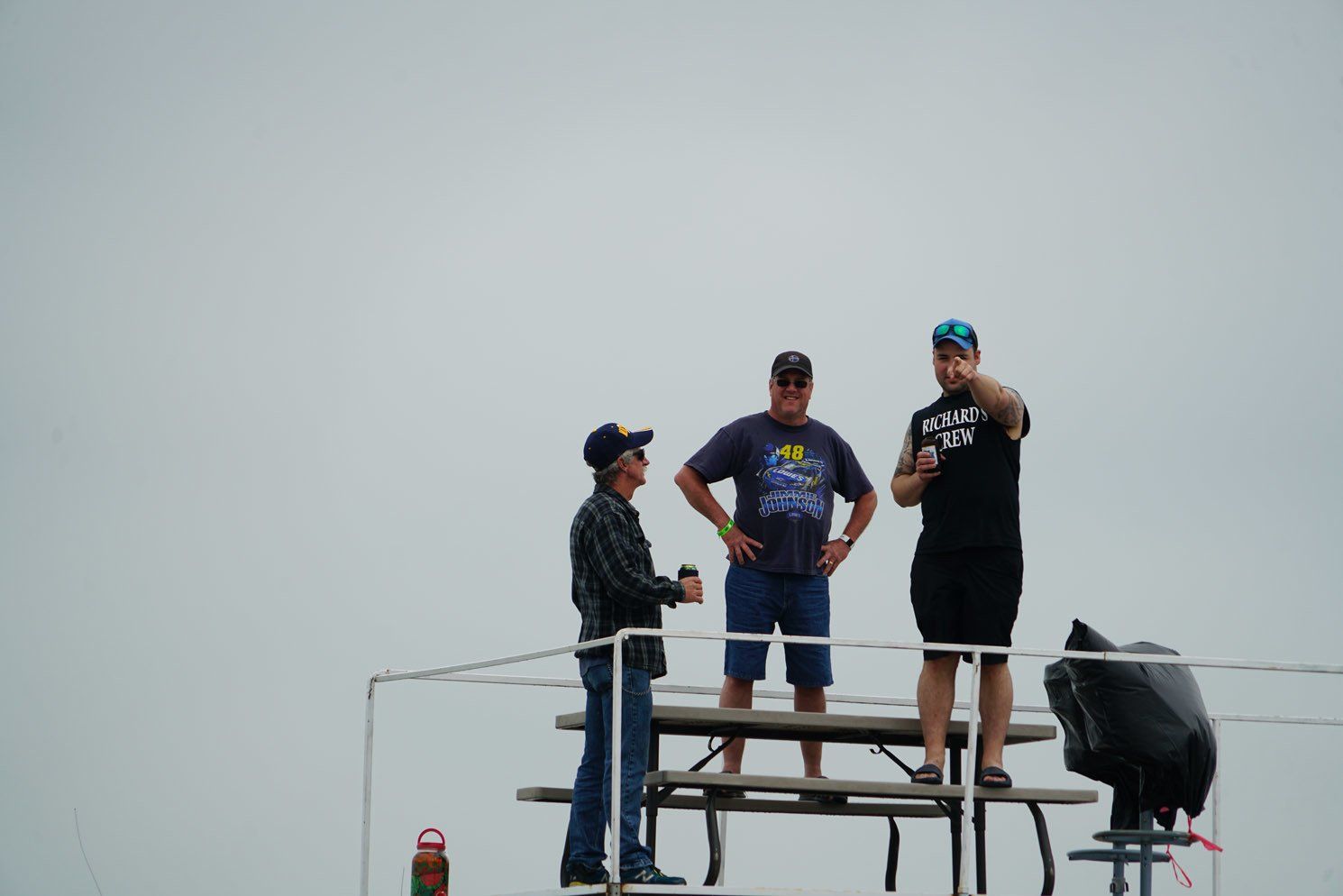 Three men are standing on top of a picnic table.