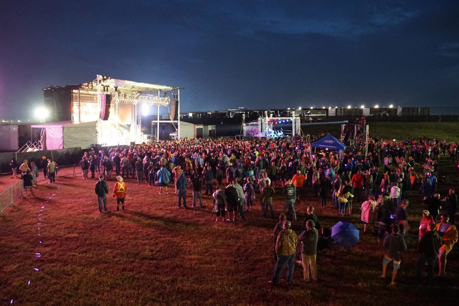 A large crowd of people are standing in a field at a concert.