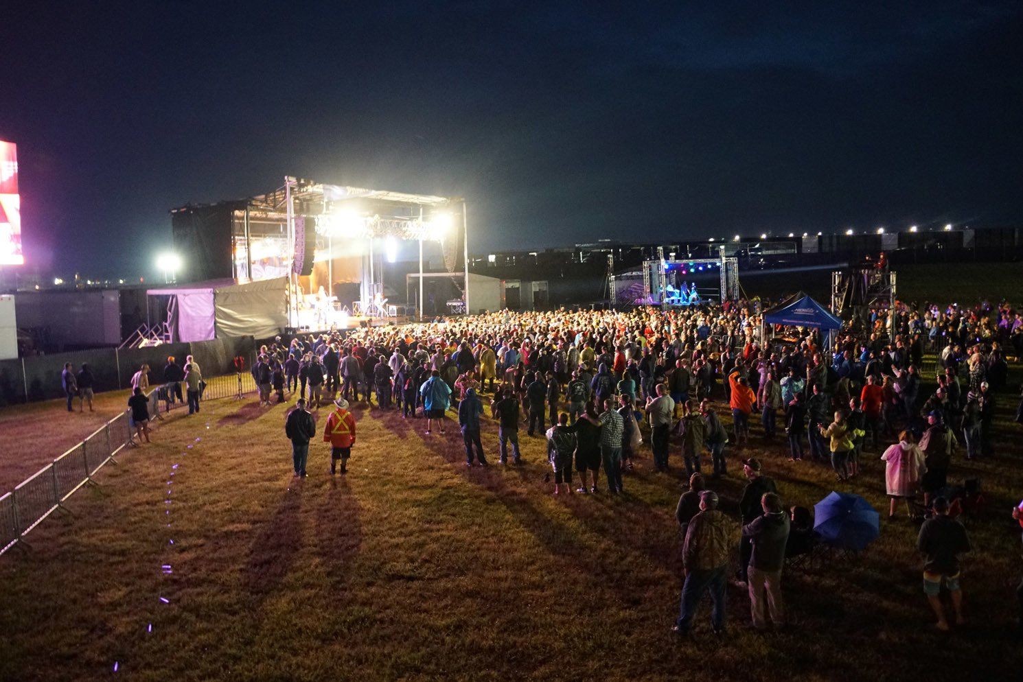 A crowd of people standing in front of a stage at a concert at night.