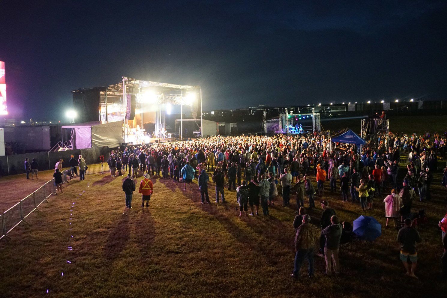 A crowd of people standing in front of a stage at a concert at night.