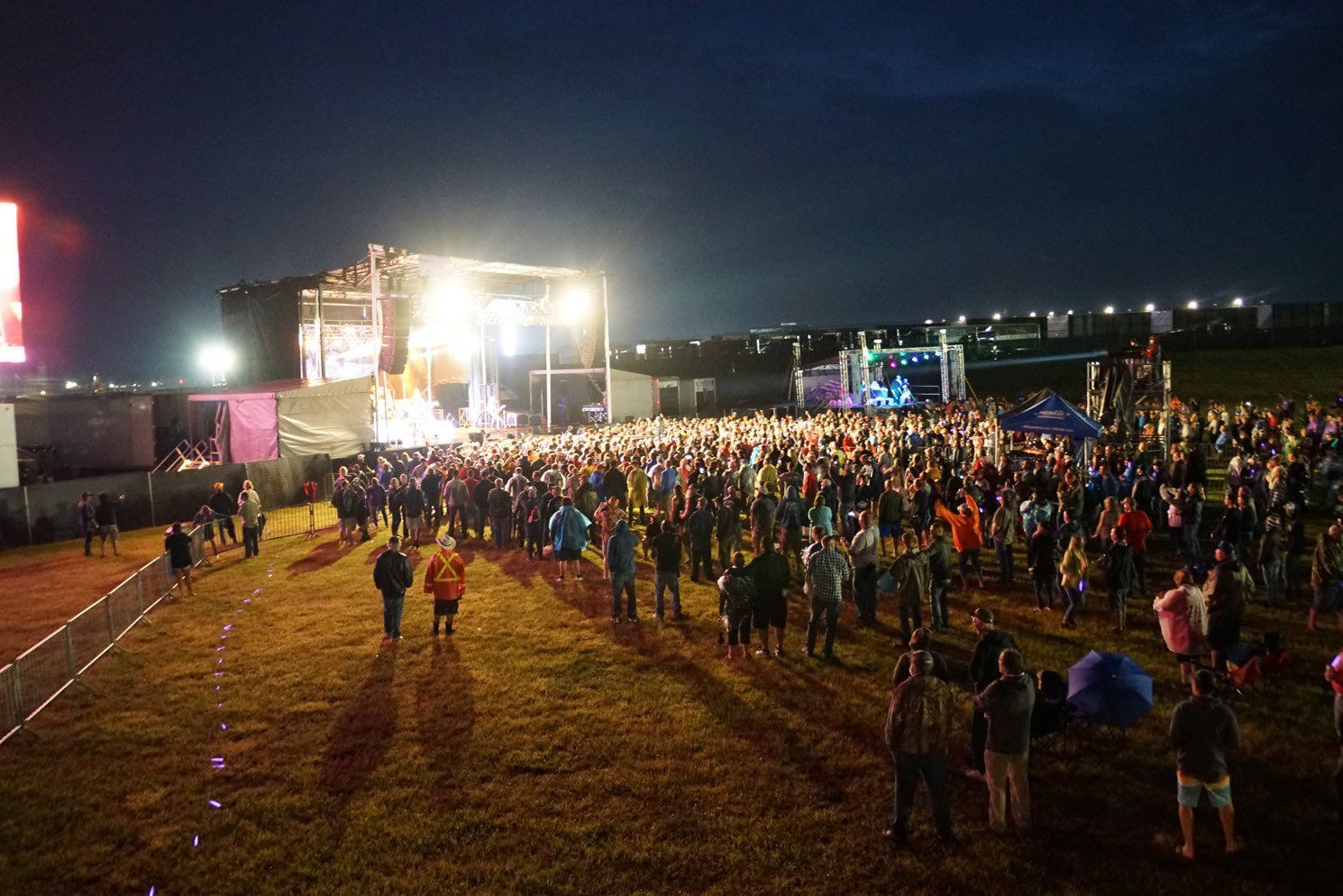A crowd of people are standing in a field at a concert at night.