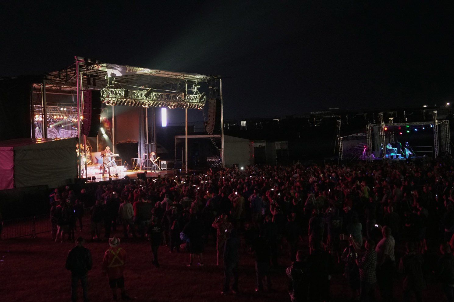 A crowd of people are standing in front of a stage at a concert at night.