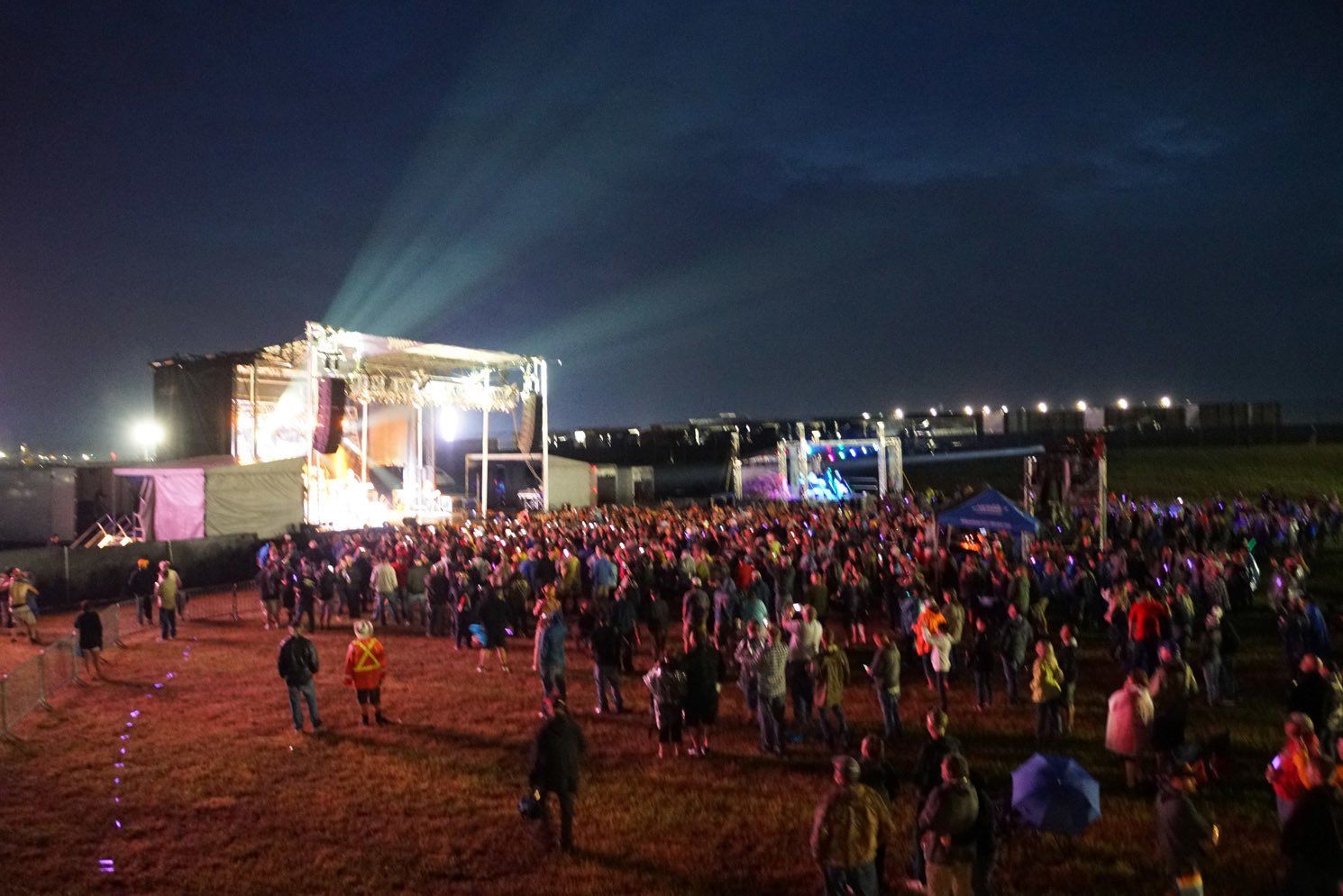 A crowd of people are standing in front of a stage at a music festival at night.