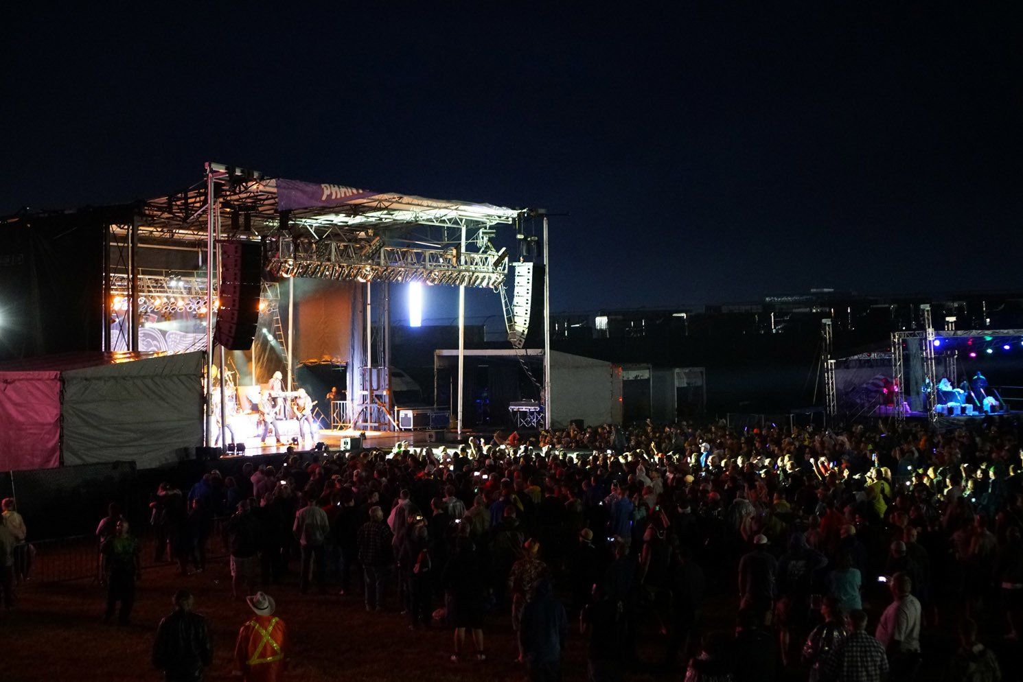 A crowd of people are standing in front of a stage at a concert at night.