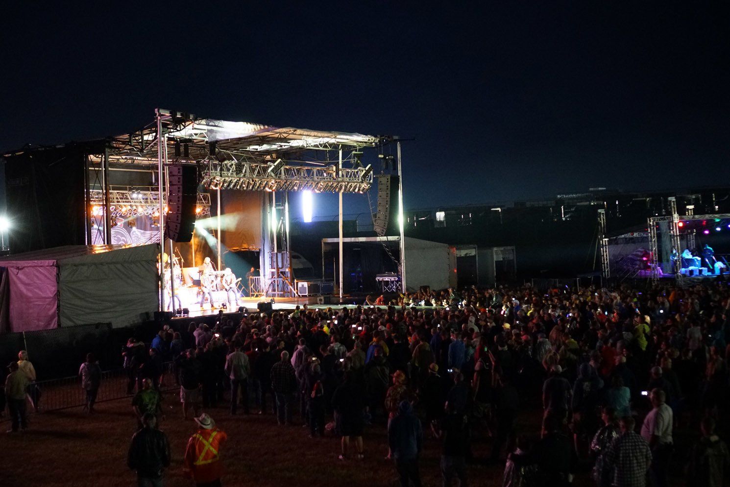 A crowd of people are standing in front of a stage at a concert at night.