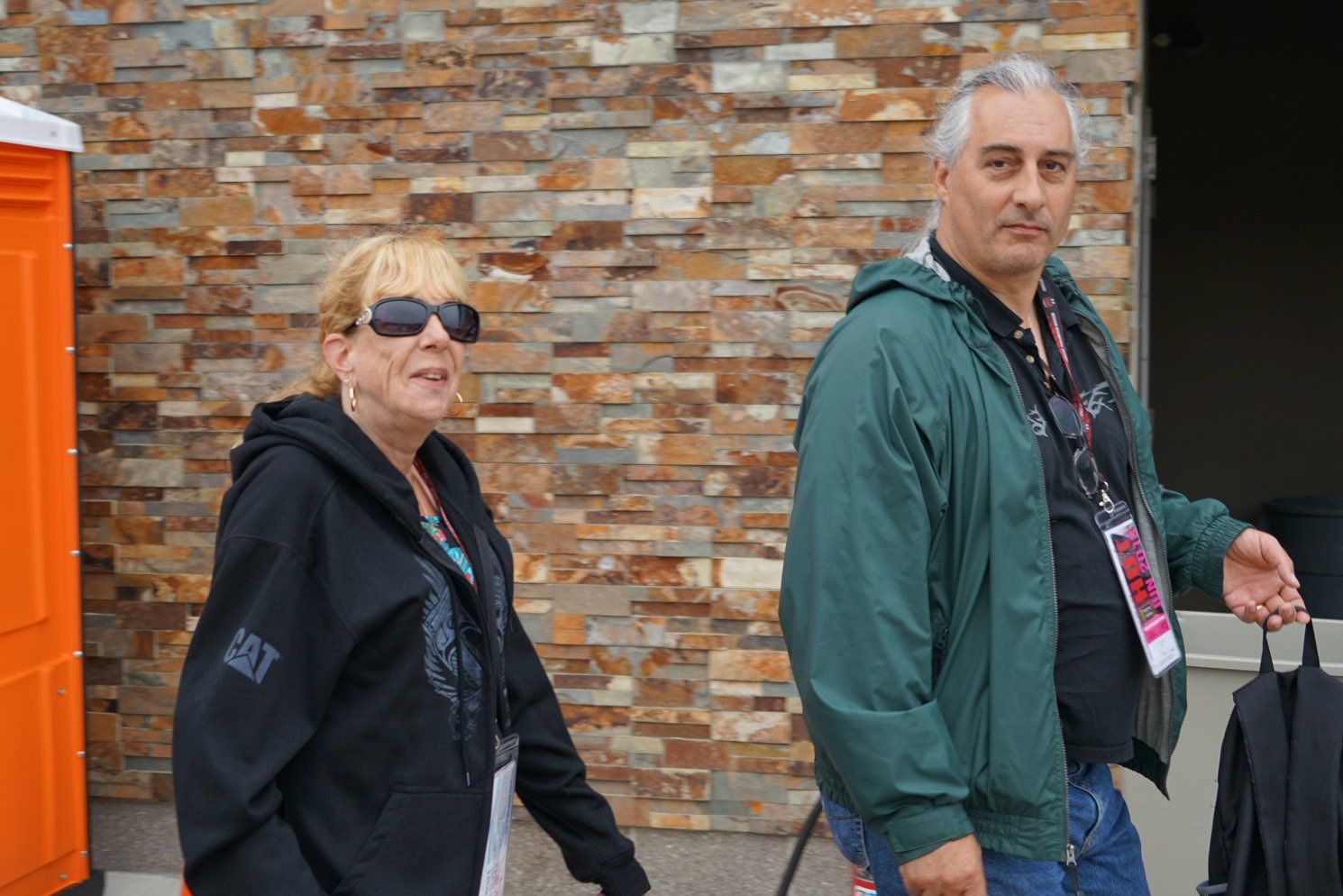 A man and a woman are standing next to each other in front of a brick wall.
