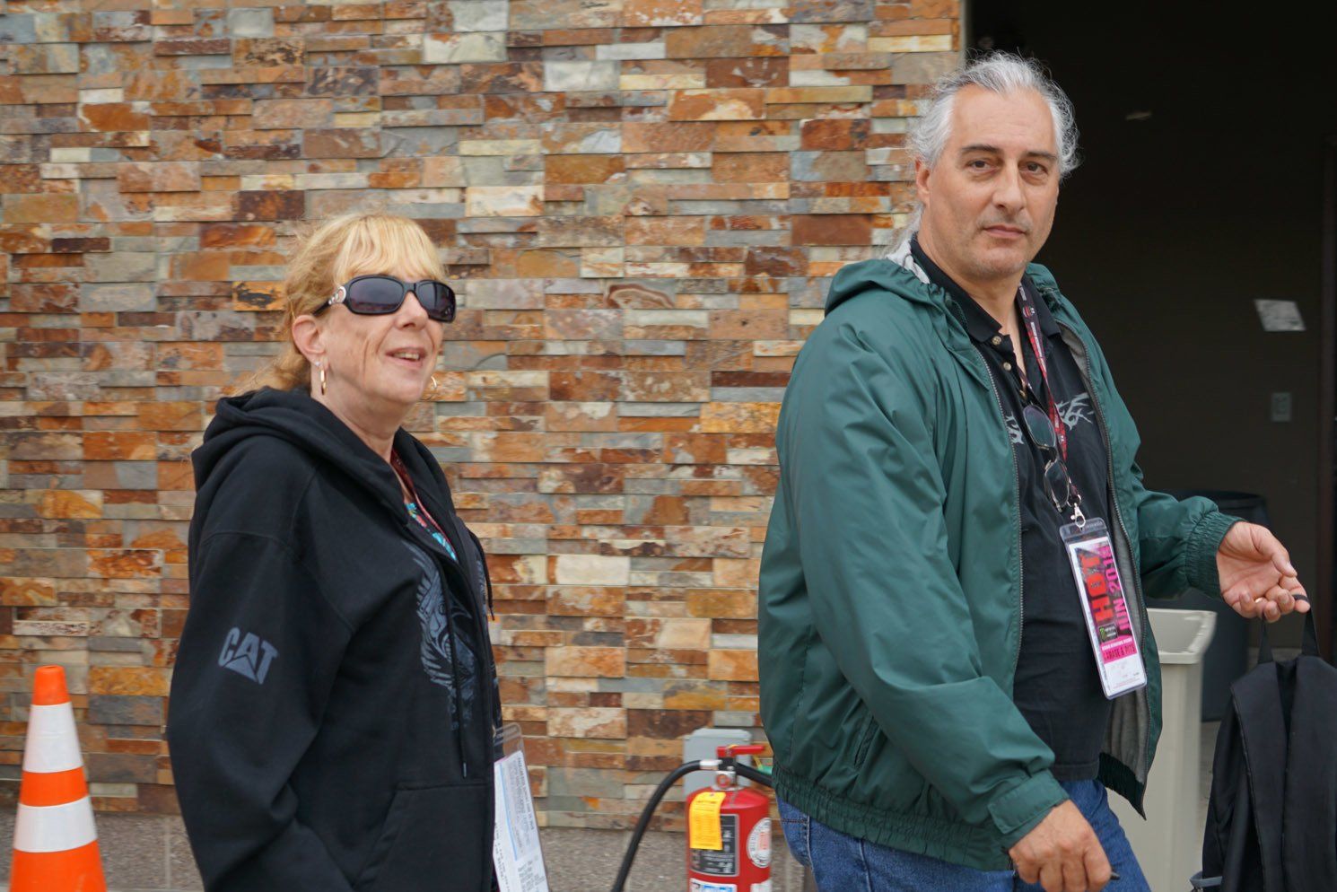 A man and a woman are walking in front of a brick wall.