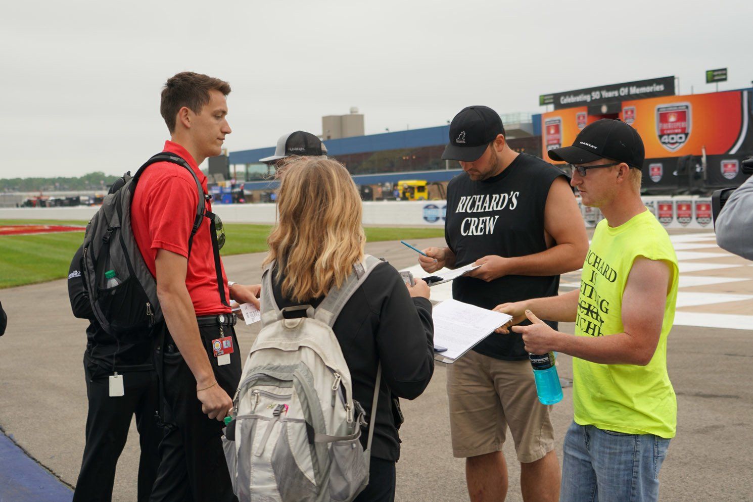 A man in a richard 's crew shirt is talking to a group of people