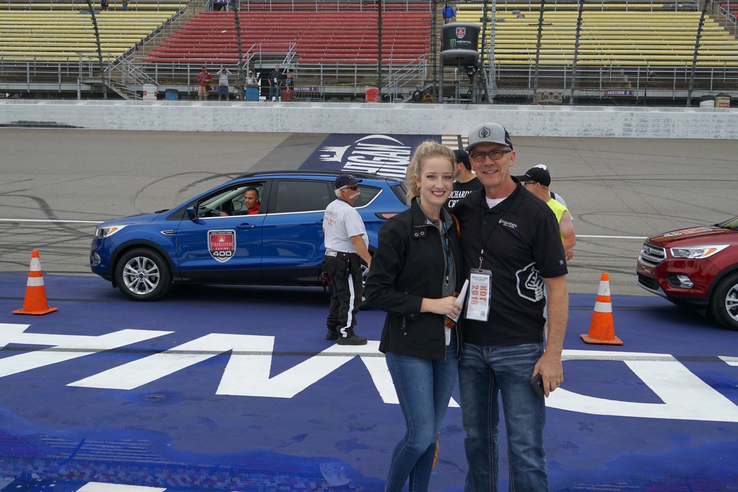 A man and a woman are standing in front of a blue car on a race track