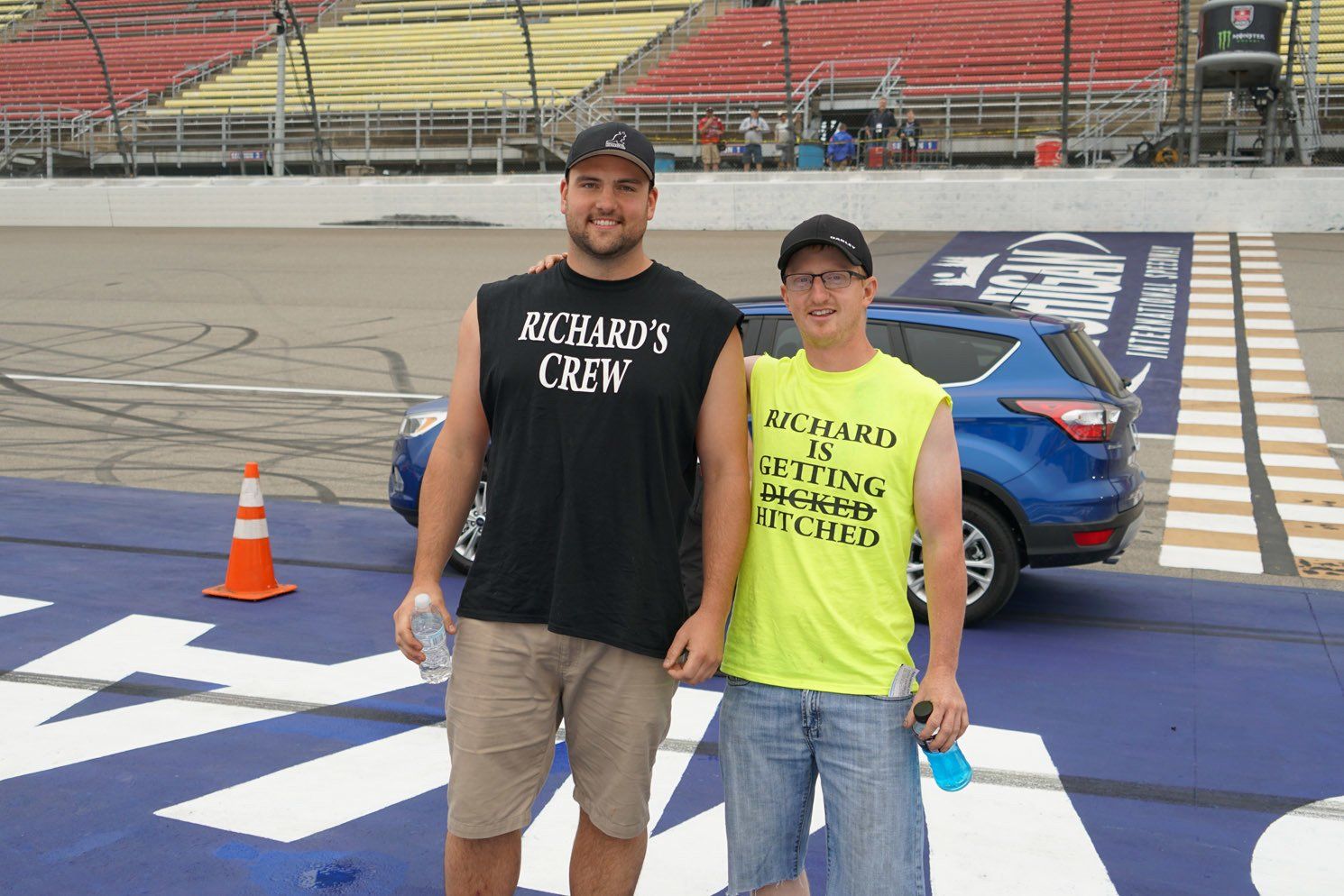 Two men standing on a race track wearing shirts that say richard 's crew