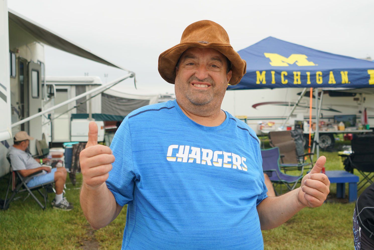 A man wearing a blue shirt that says chargers is giving a thumbs up