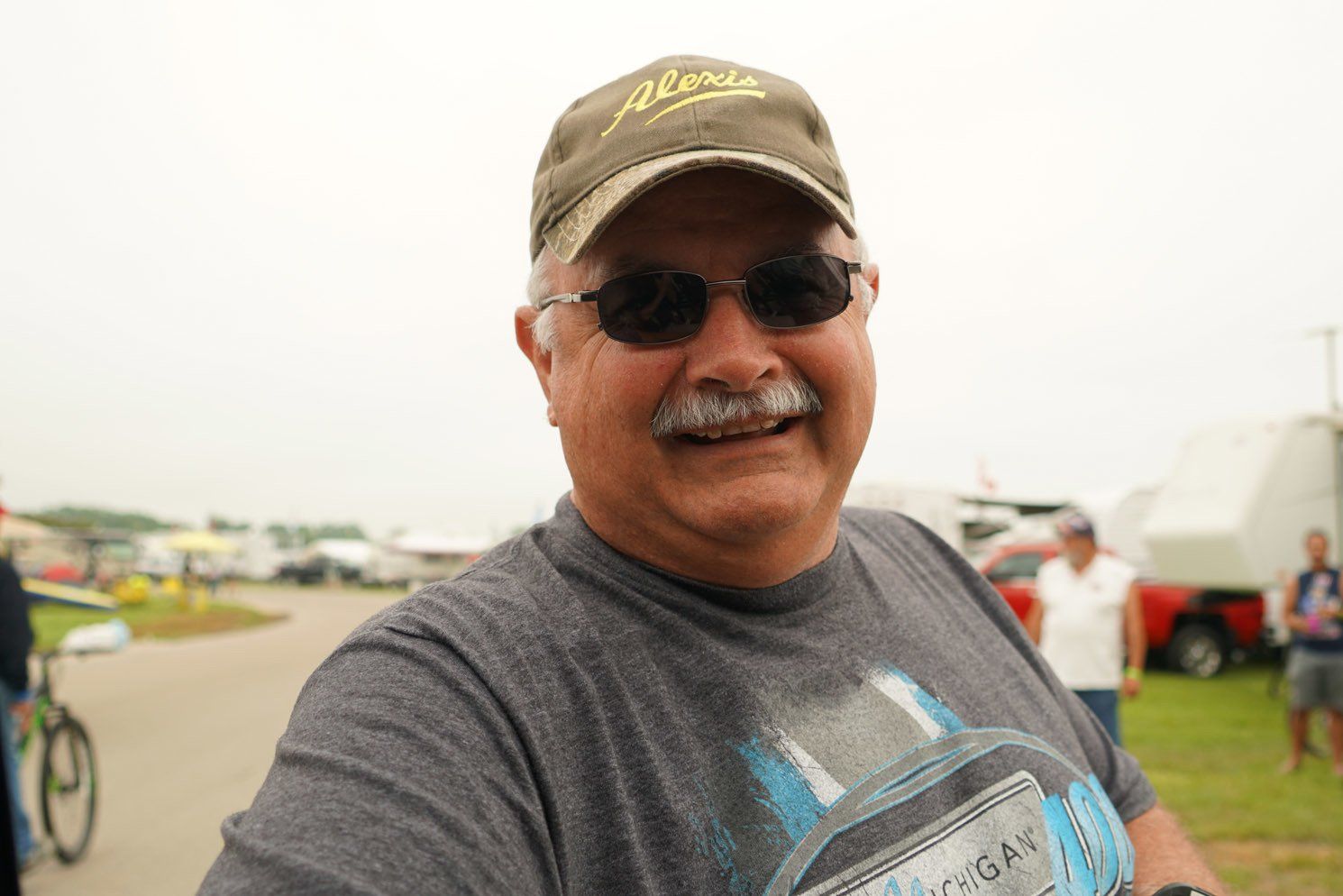 A man wearing a hat and sunglasses is smiling for the camera