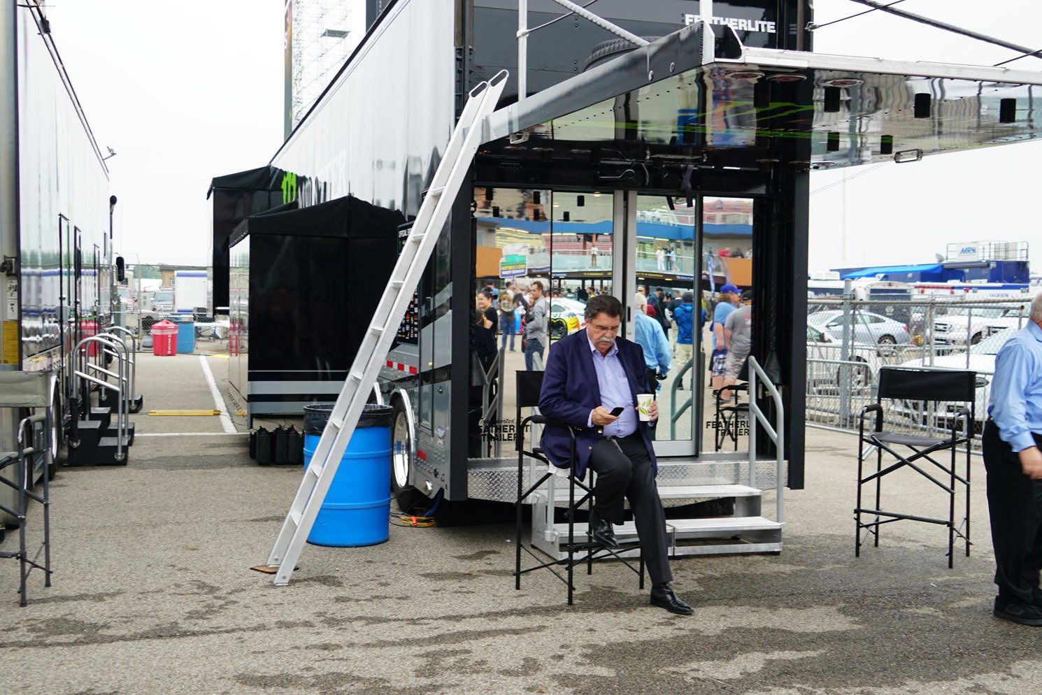 A man is sitting in front of a trailer looking at his phone.