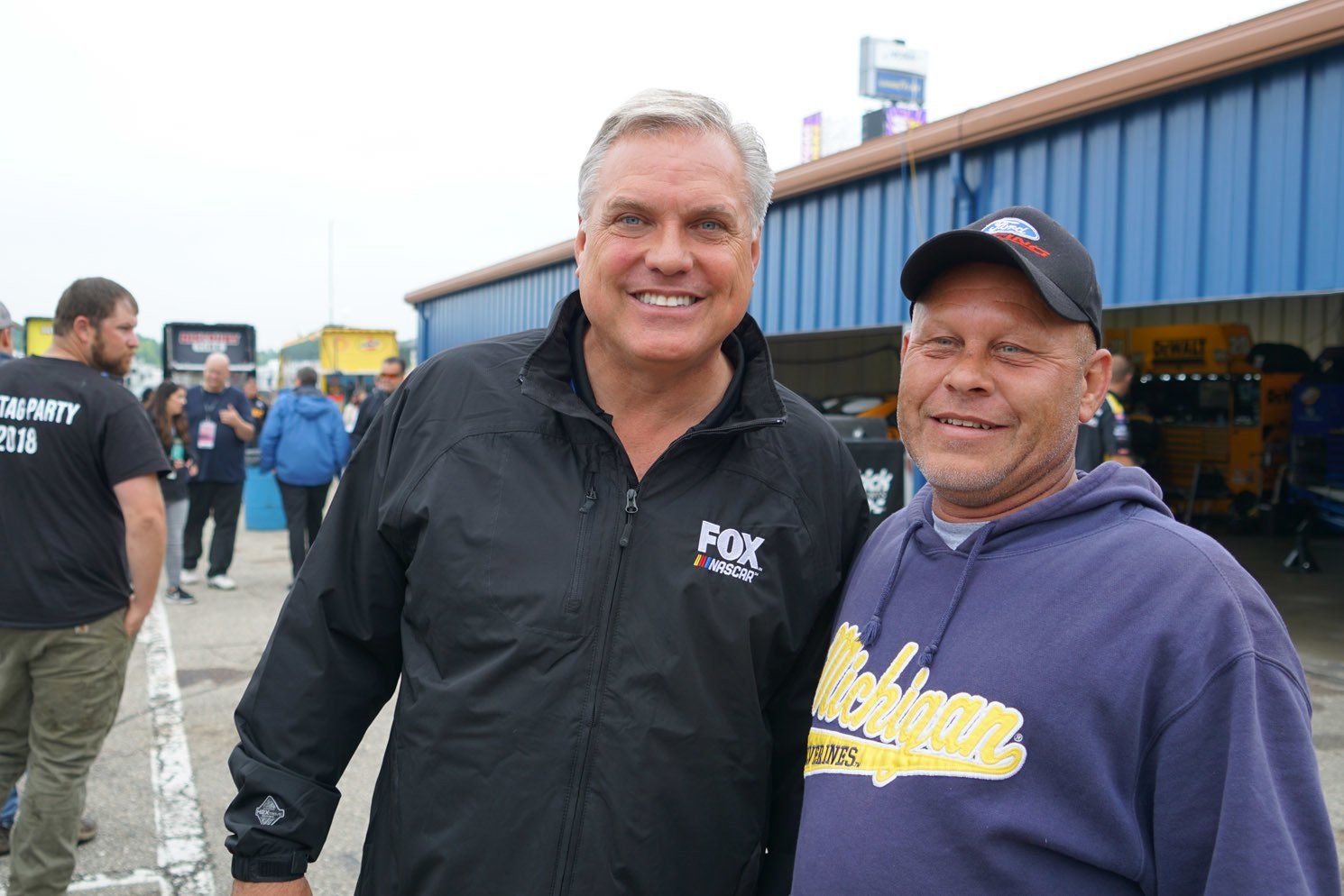 Two men are posing for a picture with one wearing a michigan sweatshirt