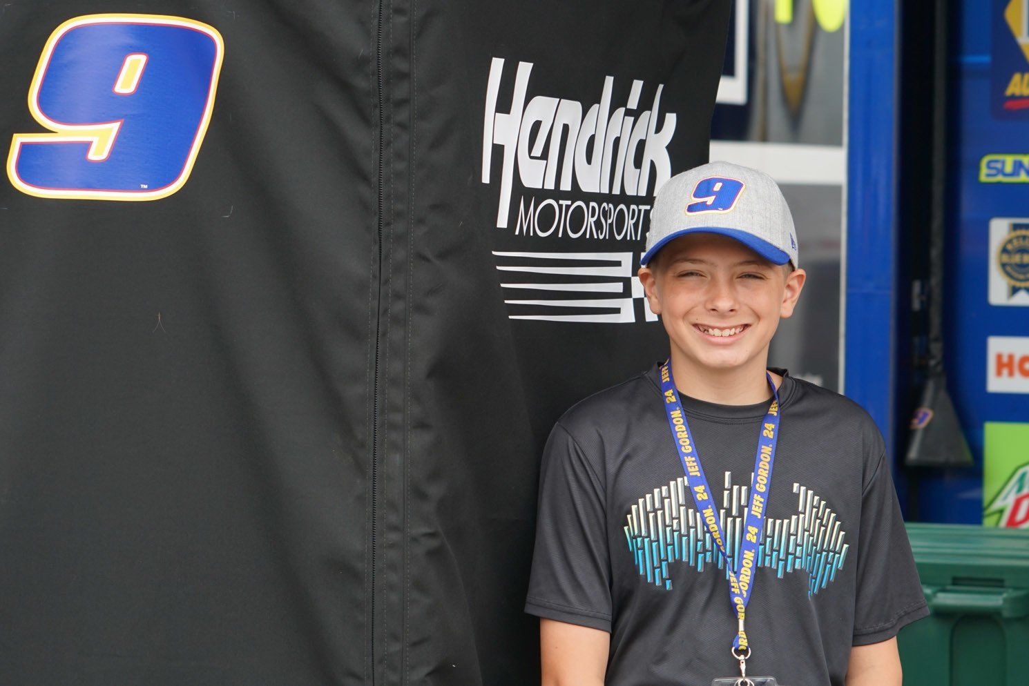 A young boy stands in front of a hendrick motorsports sign