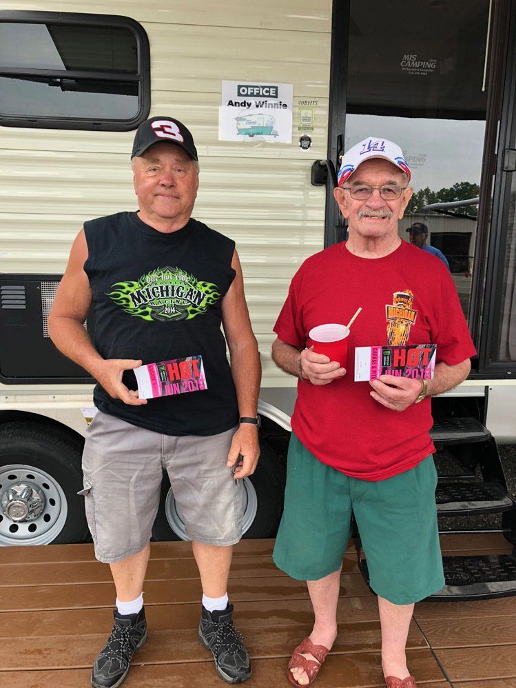 Two men are standing next to each other in front of a trailer.