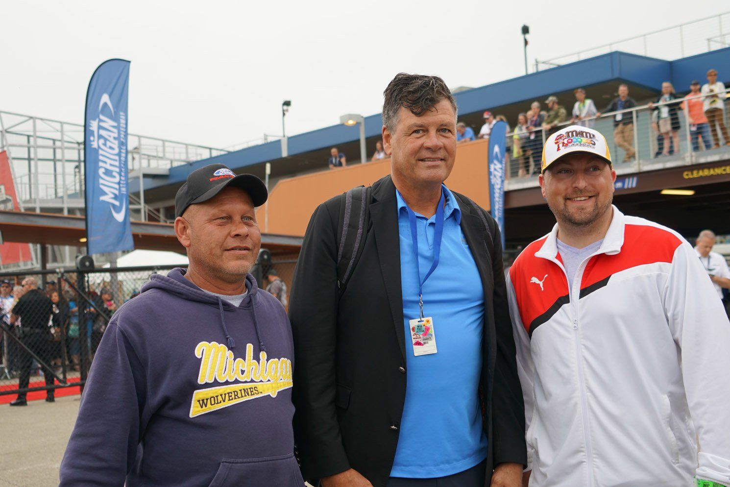 Three men are posing for a picture with one wearing a michigan sweatshirt