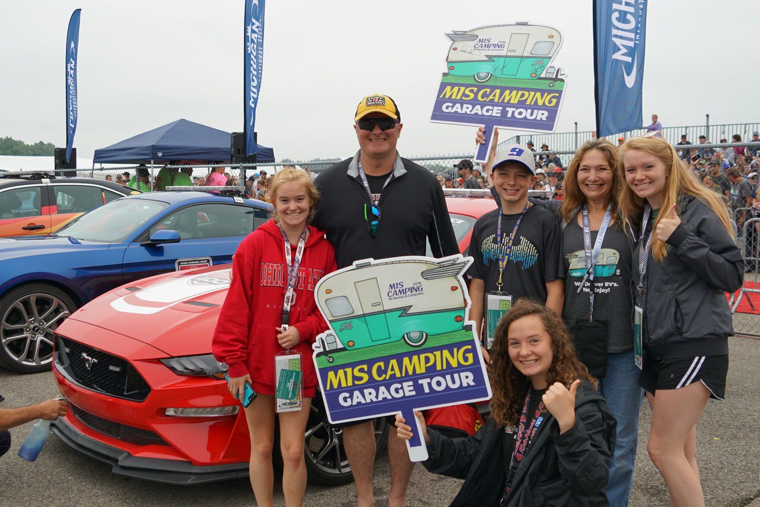 A group of people are posing for a picture in front of a red car.
