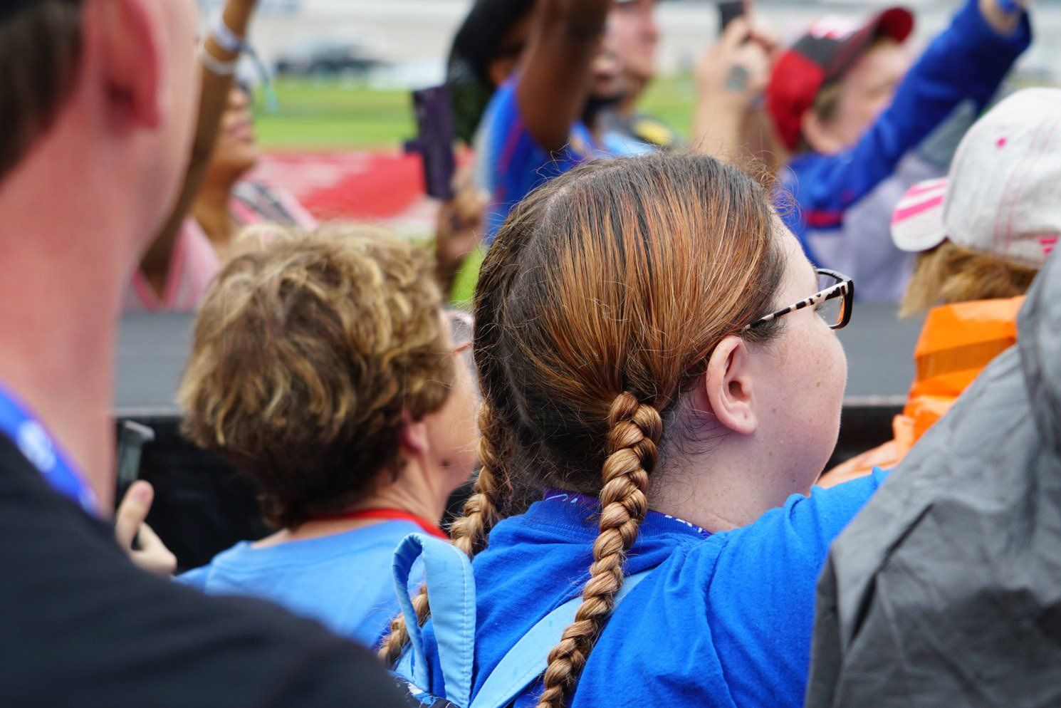 A girl with pigtails and glasses is sitting in a crowd of people.