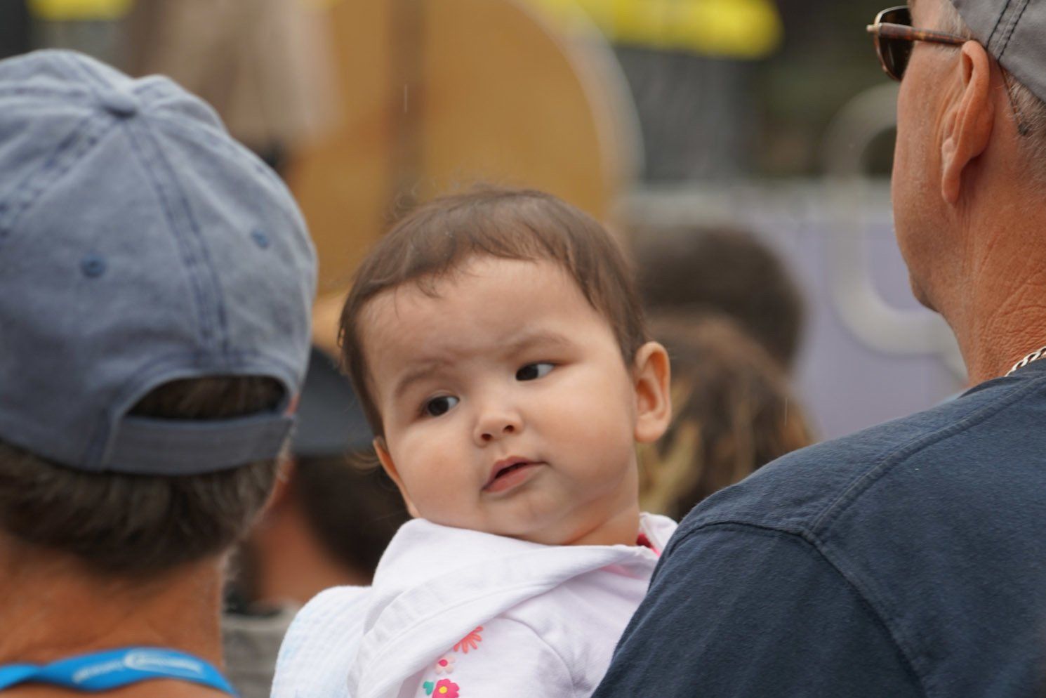 A baby is being held by a man in a blue hat