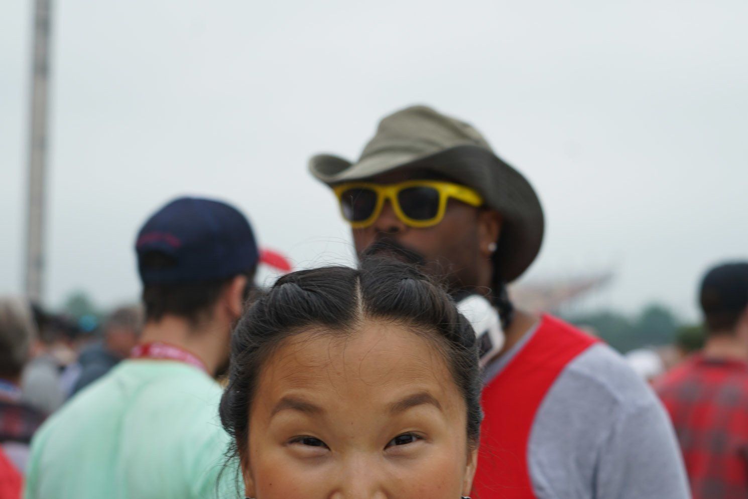 A girl wearing sunglasses and a cowboy hat stands in a crowd