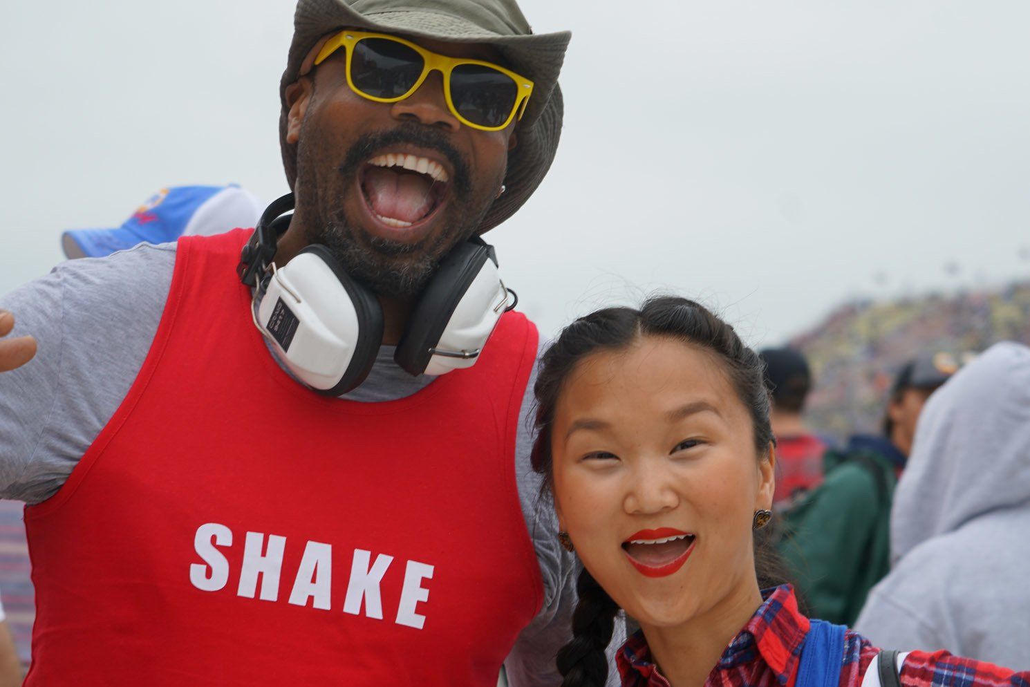 A man wearing headphones and a red shirt that says shake is posing for a picture with a woman.