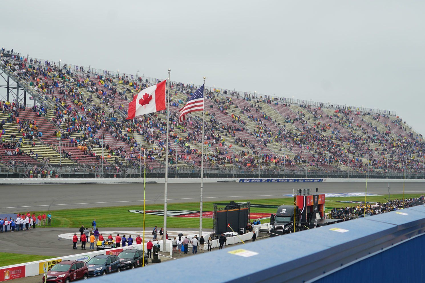 A canadian flag and an american flag are flying on a race track.