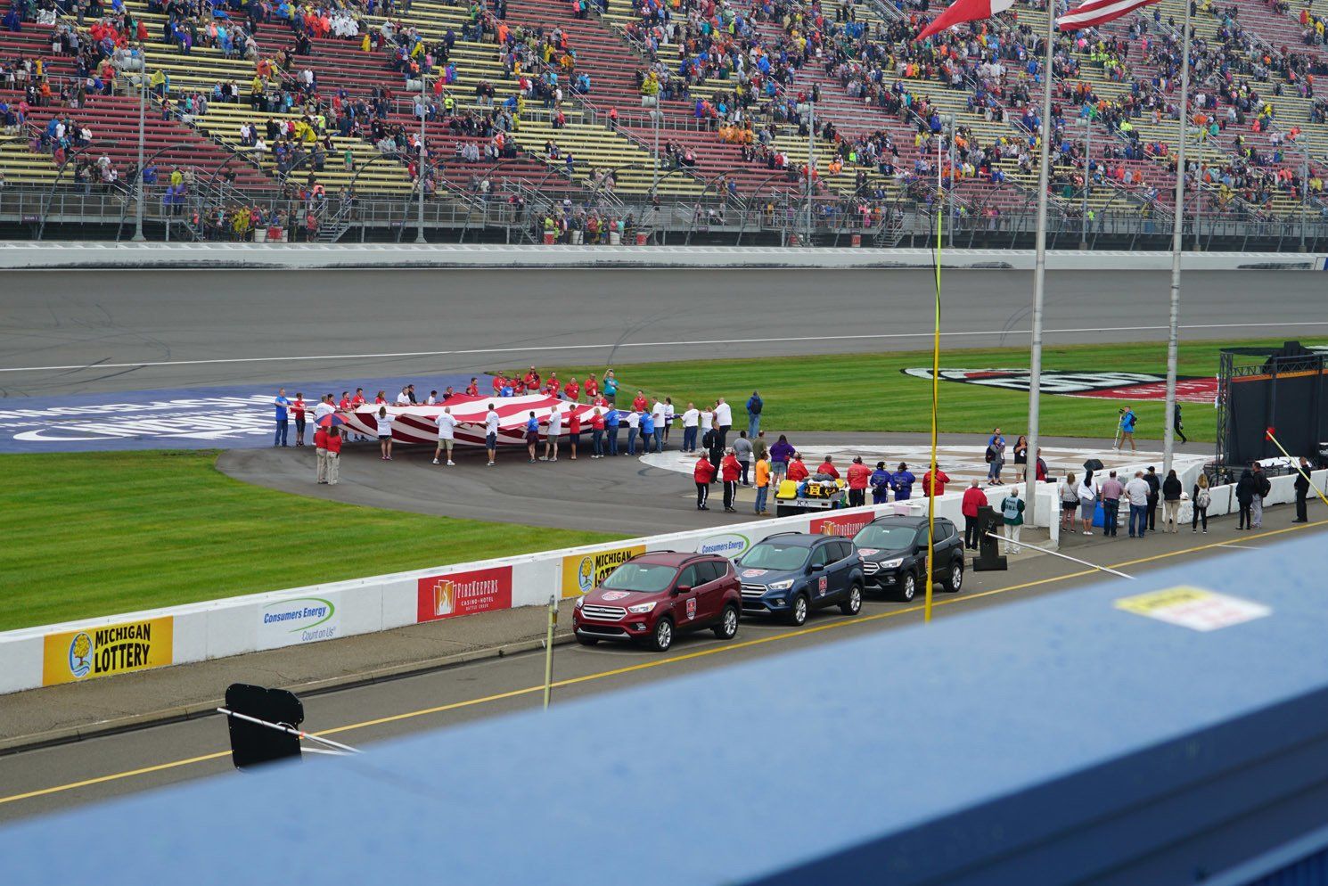 A row of cars are parked on the side of a race track