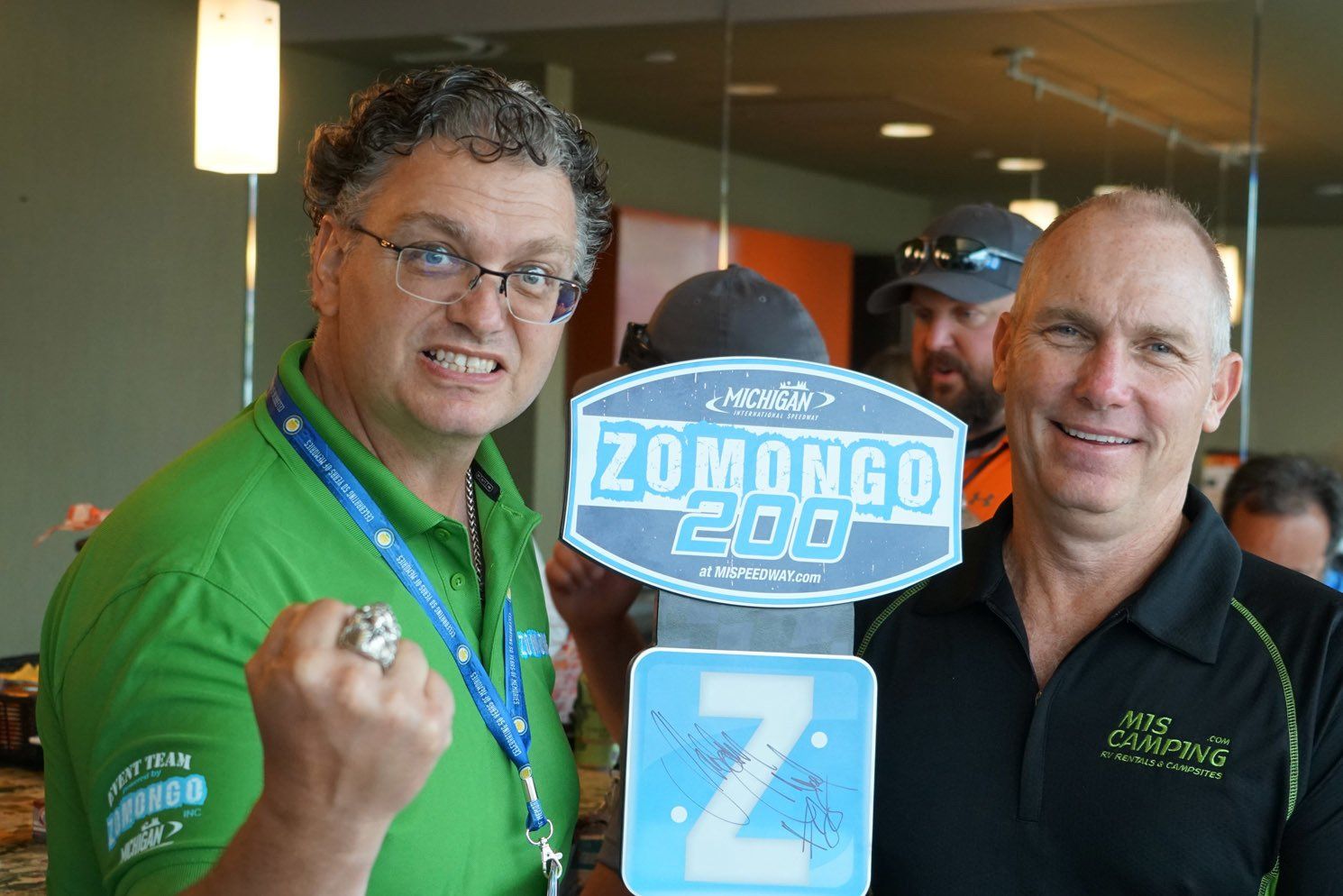 Two men holding a sign that says zomongo 200