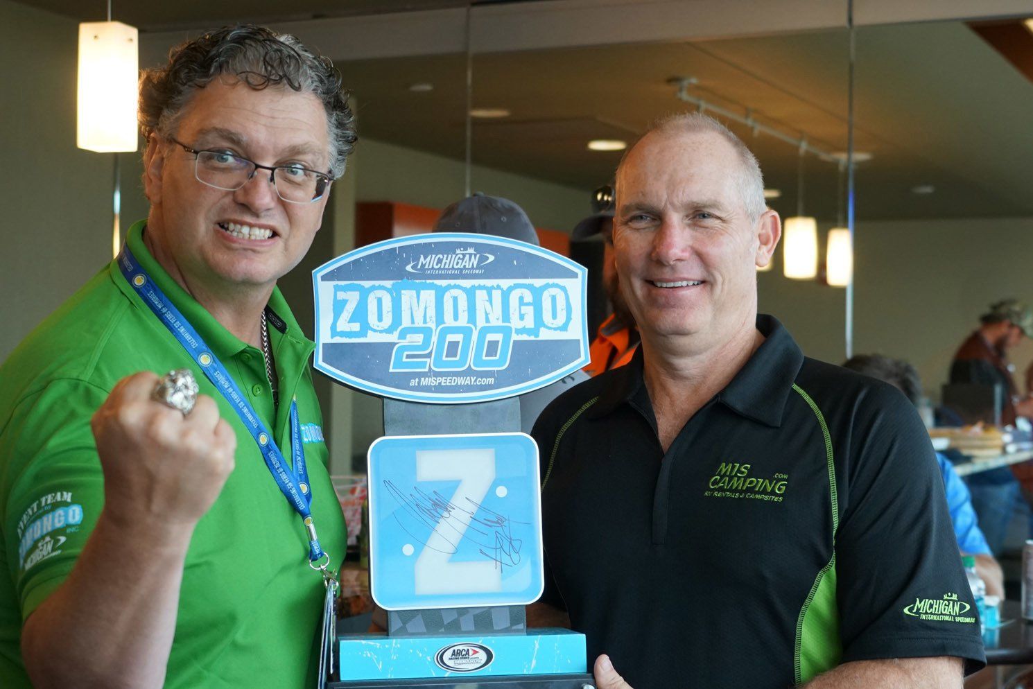 Two men holding a sign that says zomongo 200