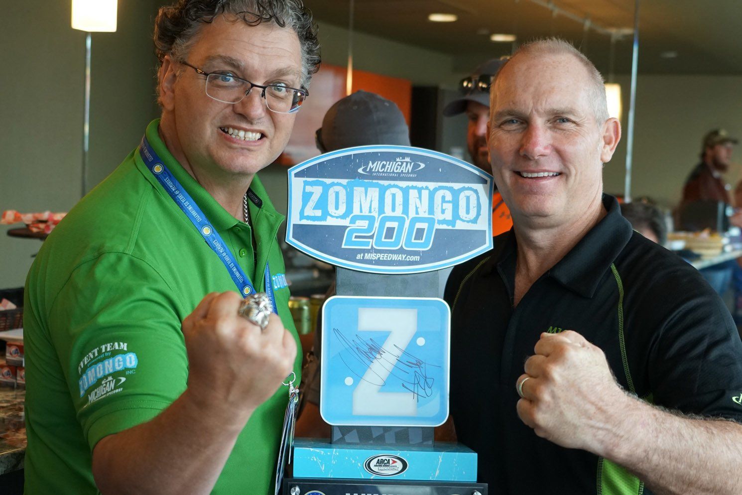 Two men standing next to a zomongo 200 sign