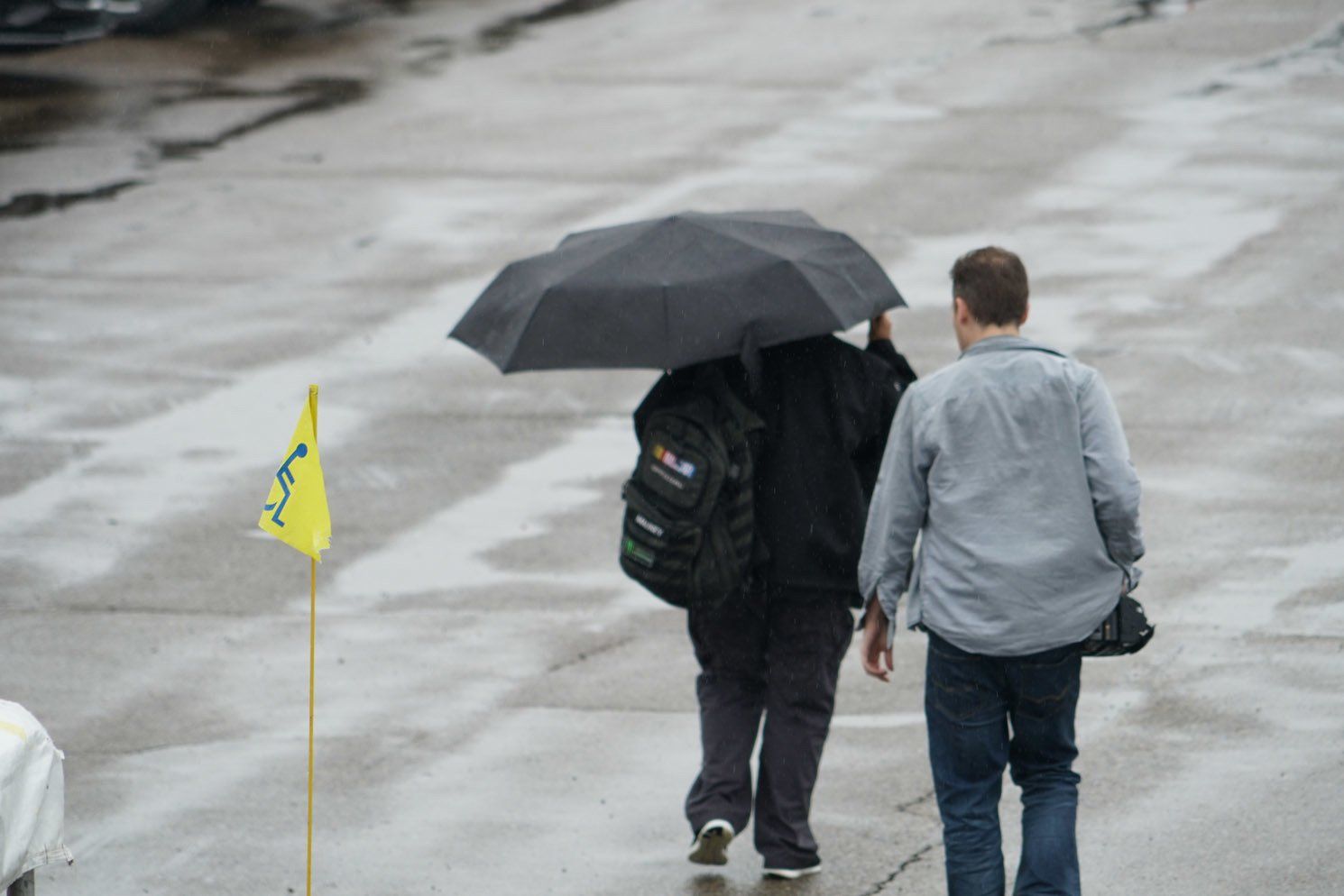 Two men are walking in the rain with an umbrella