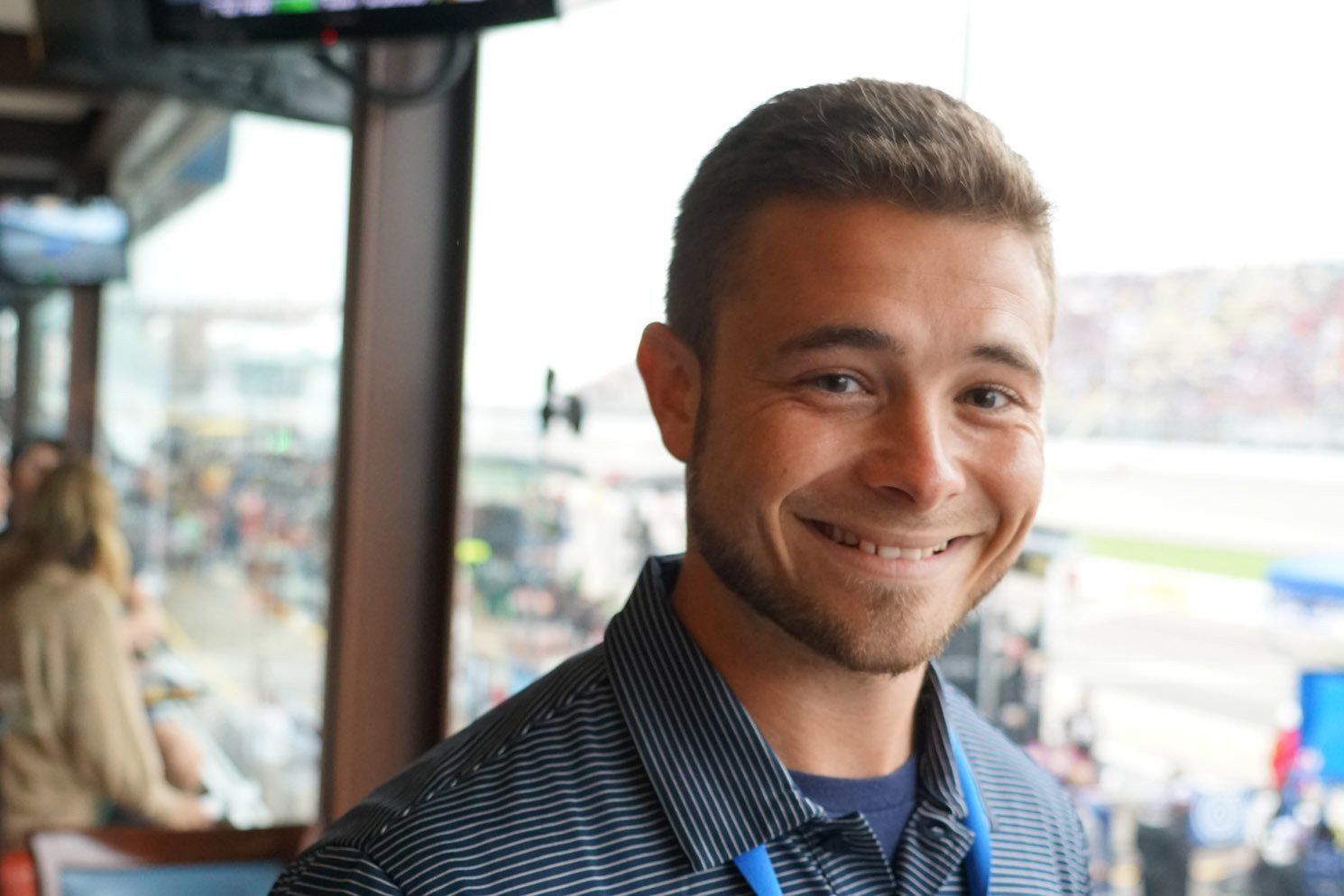 A man in a striped shirt is smiling in front of a window.
