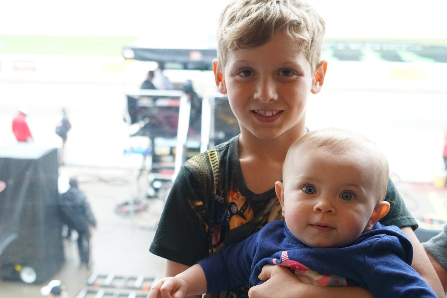 A young boy is holding a baby in his arms.