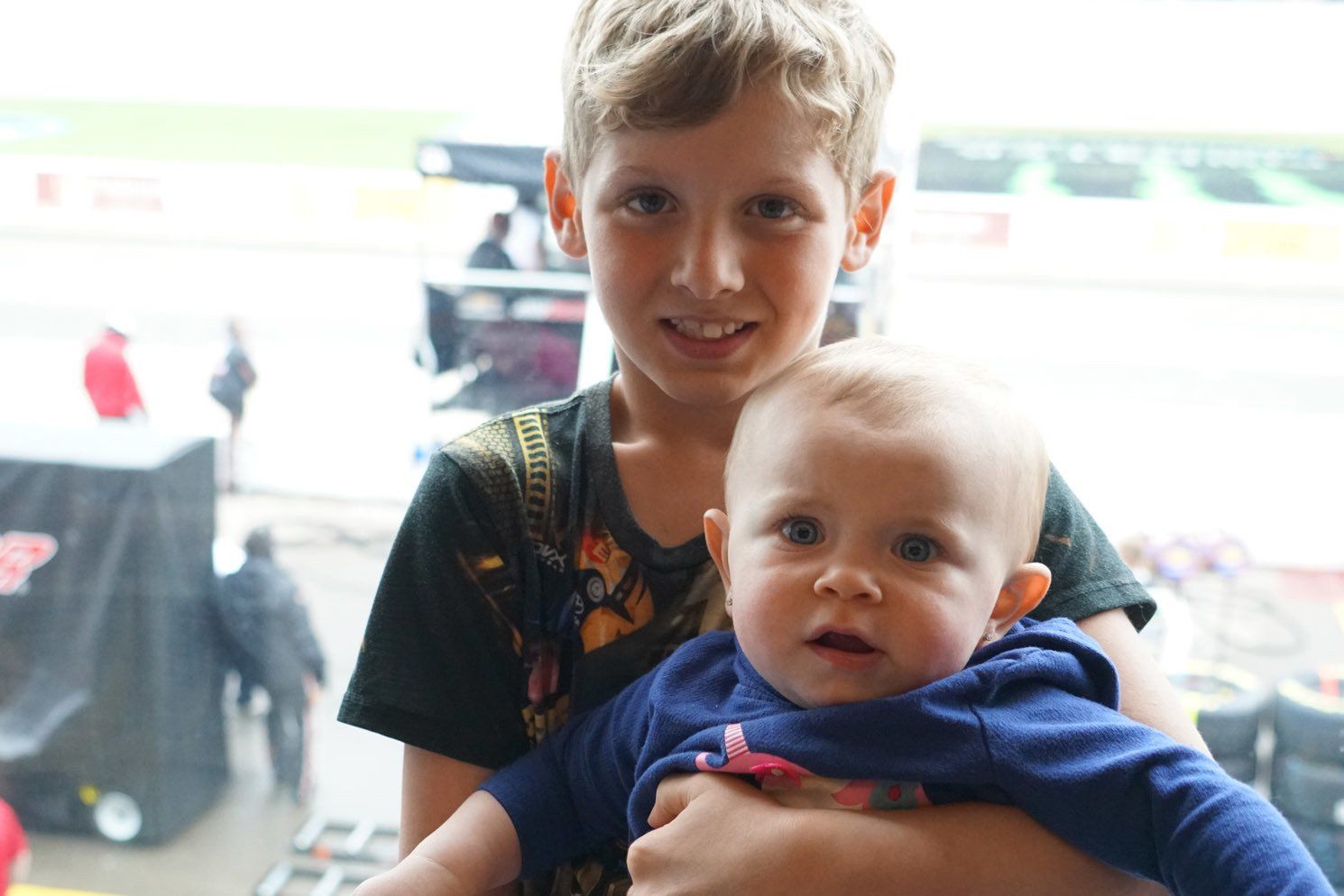 A young boy is holding a baby in his arms.