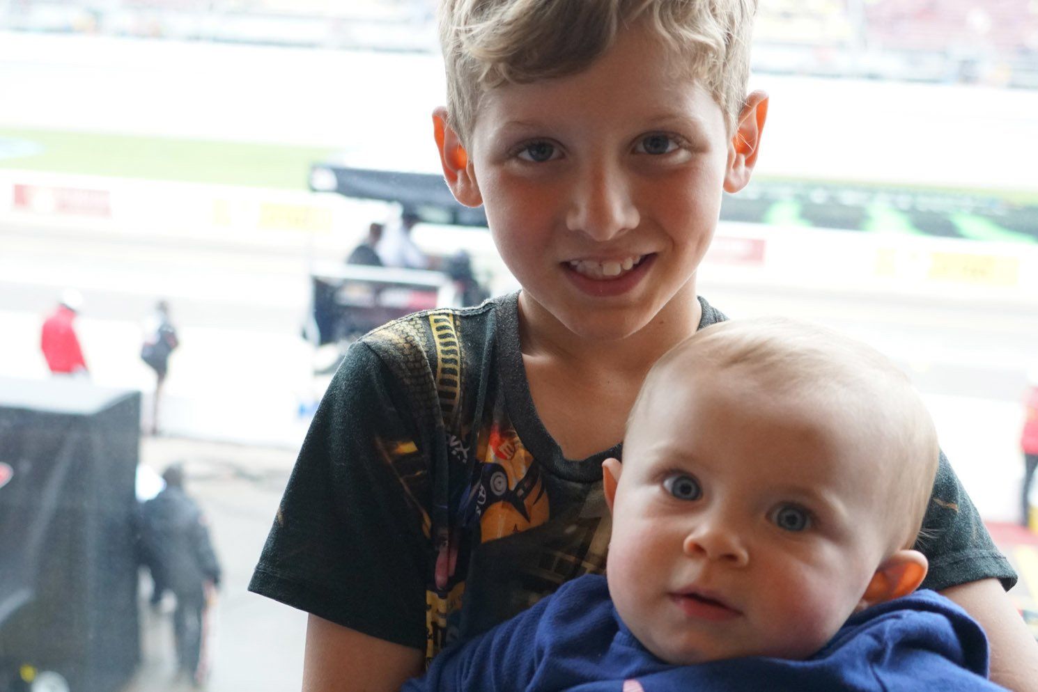 A young boy is holding a baby in his arms.