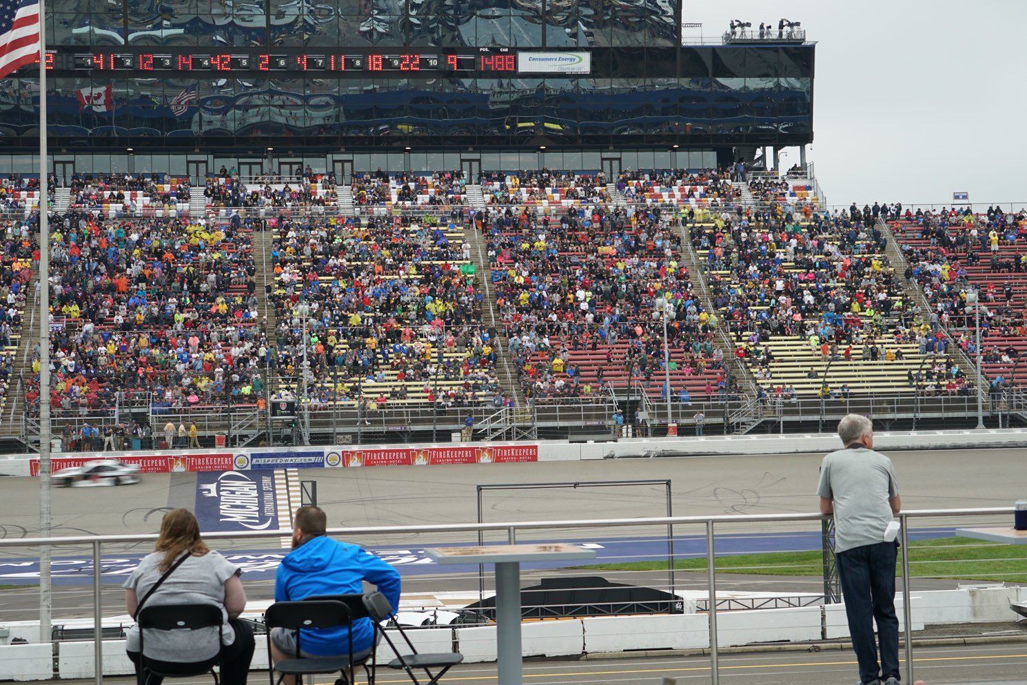 Two people are sitting in chairs at a race track watching a race.