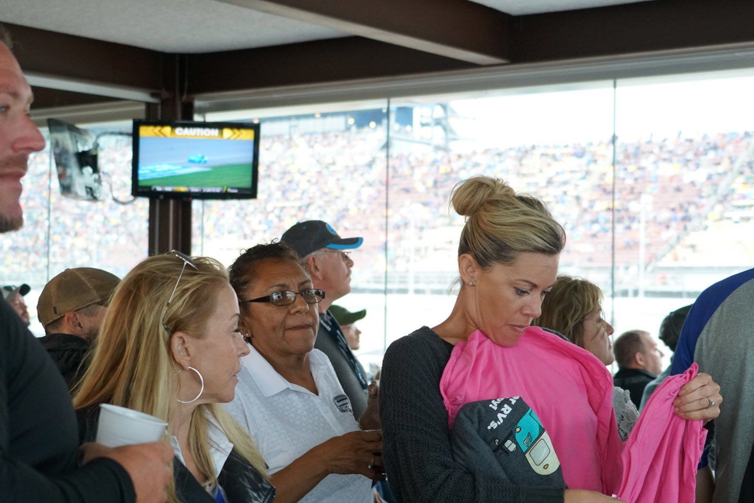 A group of people are gathered in a room with a tv on the wall