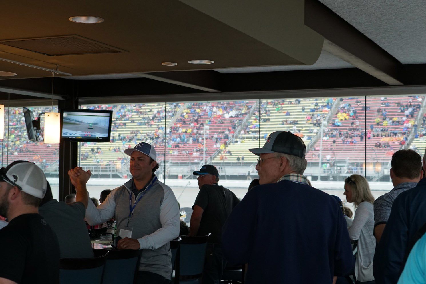 A group of people are sitting at tables in a room with a view of a race track.
